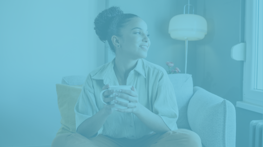 Picture of lady sitting down holding a cup, looking out of the window.